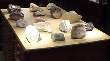Foto contendo vários tipos de minerais e rochas dispostos sobre uma mesa de madeira.
